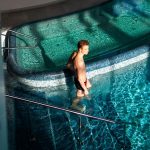 A man wades in a sunlit swimming pool, enjoying a relaxing moment with light reflections.