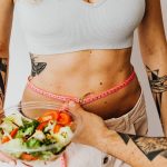 Fit woman measuring waist while holding a healthy salad bowl