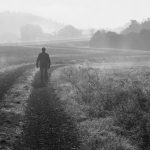 A lone person walks on a misty path in a serene black and white landscape at dawn.